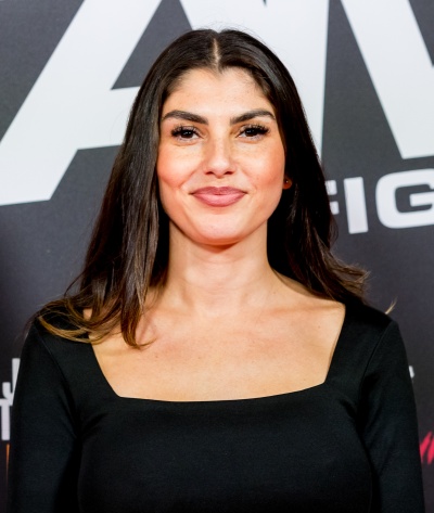 Portraitaufnahme von Yeliz Koç in einem schwarzen Kleid vor einer Logowand.