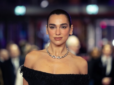Dua Lipa in einem schulterfreien Kleid mit streng zurückfrisierten Haaren. Um den Hals trägt sie eine Kette in Form einer Schlange.