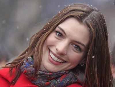 Anne Hathaway mit Schneeflocken im Haar. Sie lächelt und trägt Winterkleidung.